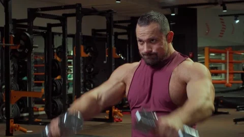 Bodybuilder performs exercise with dumbbells on muscles of the shoulders and Video stock 185631943