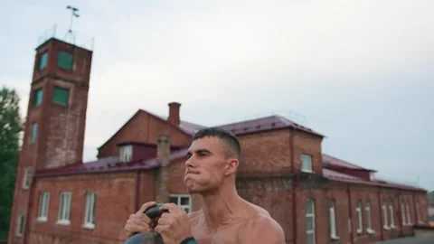 Bodybuilder performs strength exercises while standing on roof of building and Stock-Footage 247115922