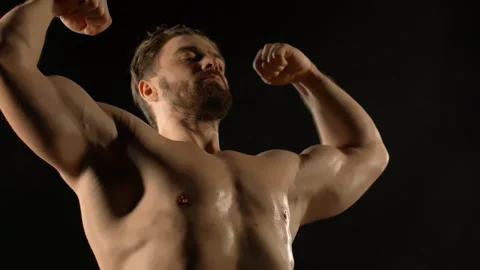 A bodybuilder poses against a black background Stock Footage 323389010