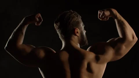 A bodybuilder poses against a black background Stock Footage 323389045
