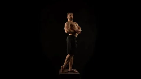 A bodybuilder poses against a black background Stock Footage 323389213