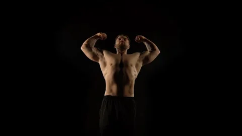 A bodybuilder poses against a black background Stock Footage 323389232