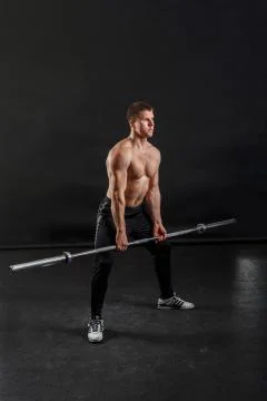 A bodybuilder is posing with barbell on his knees Stock Photos