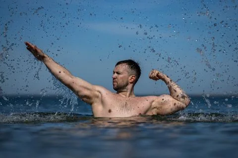 Bodybuilder posing near seaside waves. Strong bodybuilder shows muscular chest Stock Photos