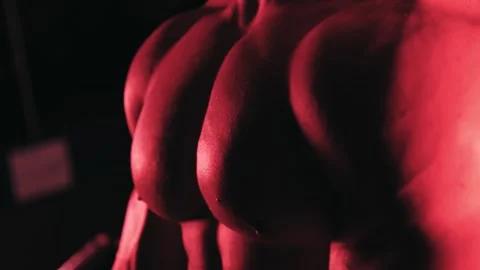 Bodybuilder posing tensing chest muscles in red light Stock Footage 132181763