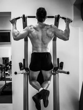 Bodybuilder pulling up on a bar in a gym 库存照片