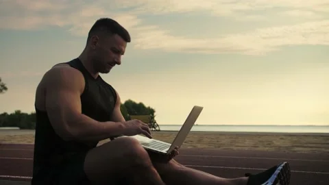Bodybuilder sits on a mat against the background of sunrise and the sea, hol Stock Footage 200118181