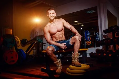 Bodybuilder sits on a weight bench, he takes a break. Muscular man at a worko Stock Photos