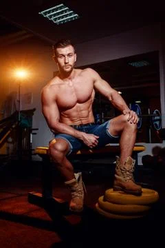 Bodybuilder sits on a weight bench, he takes a break. Muscular man at a worko Stock Photos