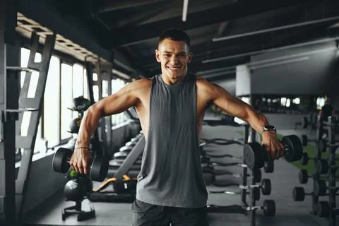 Bodybuilder smiling and looking at camera while training delts muscles with Stock Photos