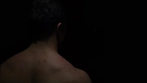 The bodybuilder stands with his back to the camera in a dark room and looks Stock Footage 130301250