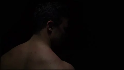 The bodybuilder stands with his back to the camera in a dark room and looks Stock Footage 130301265