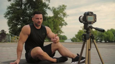 Bodybuilder talks to the camera while sitting on a mat against a background  Stock Footage 200118256