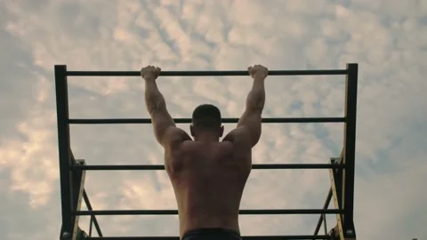 Bodybuilder is training outdoor, doing pull-ups on his back muscles. Stock Footage 200118069
