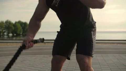 Bodybuilder training outdoors doing an exercise with fighting ropes against  Stock Footage 200118291