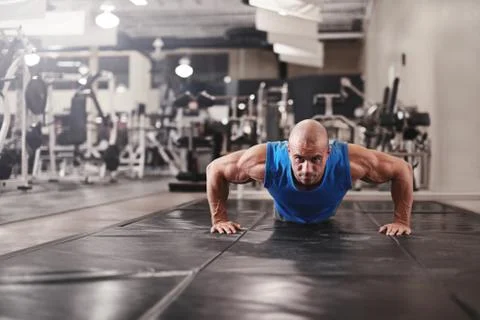 Bodybuilder working out and doing push upsat the gym while Stock Photos