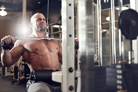Bodybuilder working out at the gym while using fitness machine Stock Photos