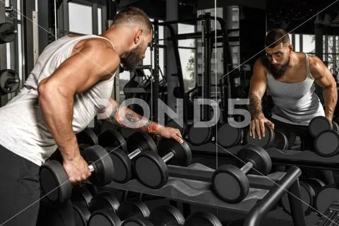 Bodybuilding. Bearded man exercising at gym with dumbbell looking at mirror Stock Photos