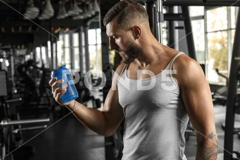 Bodybuilding. Bearded man standing at gym looking at protein shake bottle Stock Photos