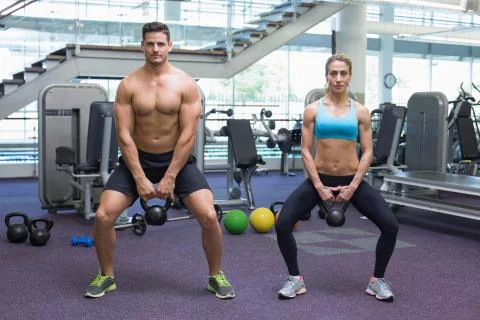 Bodybuilding man and woman lifting kettlebells in a squat Stock Photos