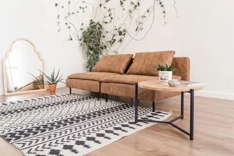 Boho style interior featuring a brown leather sofa, geometric patterned rug Foto stock