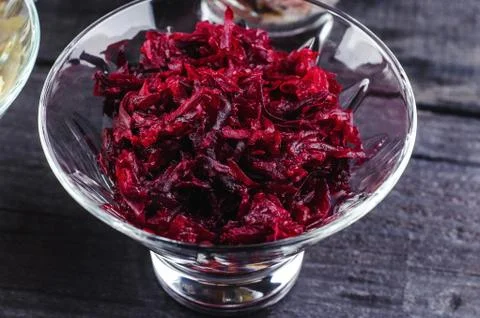 Boiled beet shredded in a transparent deep dish on a wooden black background. Stock Photos