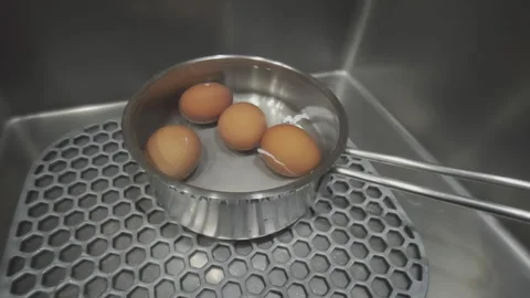 Boiled brown eggs in a pot of hot water cooling down inside a kitchen sink. One Stock Footage 344814445