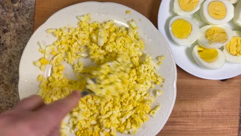 	Boiled chicken egg halves with bright yolks are mashed with a fork in a plate. Stock Footage 301332441