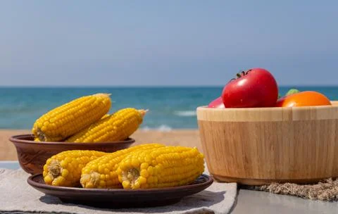Boiled corn on the cob on an earthenware plate. fresh tomatoes and cucumbers in Stock Photos