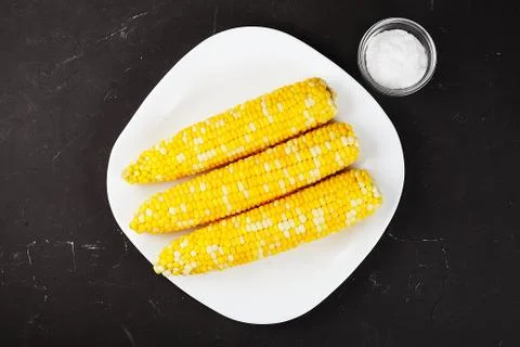 Boiled corn on a white square plate, dark table, hodgepodge with salt.. Flat Foto stock
