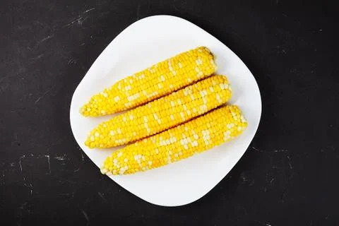 Boiled corn on a white square plate, dark table.. Top view. Stock Photos