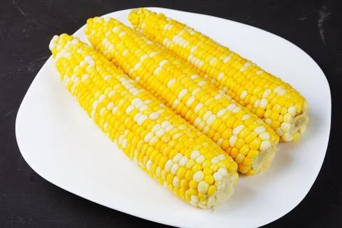 Boiled corn on a white square plate, close-up, soft focus Stock Photos