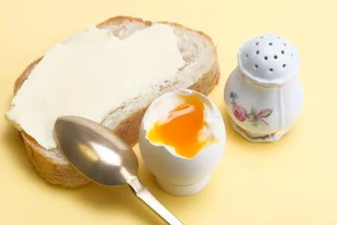 Boiled egg, bread with butter, salt cellar and brass spoon Stock Photos