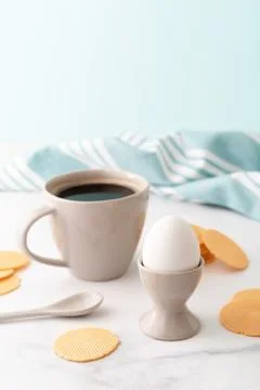 Boiled egg in ceramic egg cup, cup of coffee and thin crispy corn chips on Stock Photos