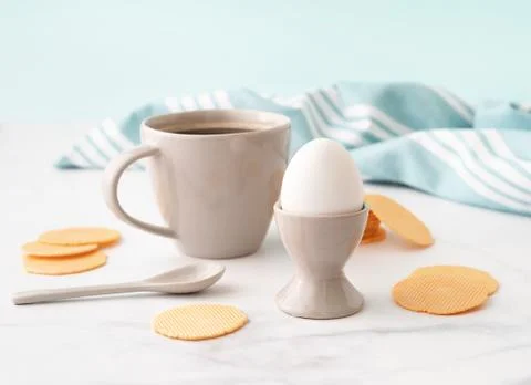 Boiled egg in ceramic egg cup, cup of coffee and thin crispy corn chips on ba Stock Photos