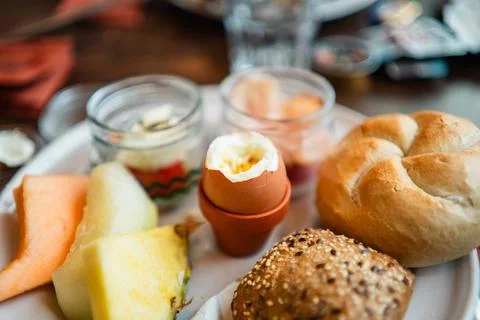 Boiled Egg Cracked Open on a Breakfast Plate with Bread Buns and Fruit Slices Stock Photos