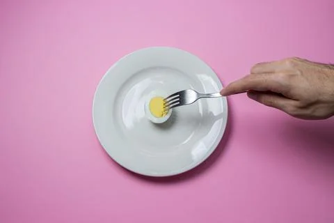 A boiled egg cut in half on a plate. The hand reaches for food. Healthy breakfas Stock Photos