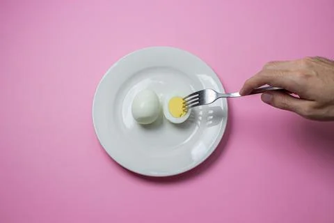 A boiled egg cut in half on a plate. The hand reaches for food. Healthy breakfas Stock Photos