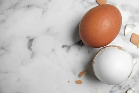 Boiled eggs and pieces of shell on white marble table, flat lay. Space for te Foto stock