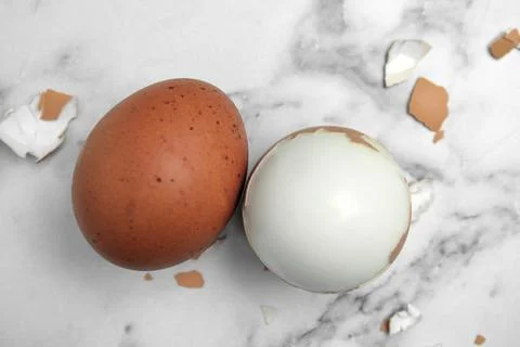 Boiled eggs and pieces of shell on white marble table, flat lay Foto stock