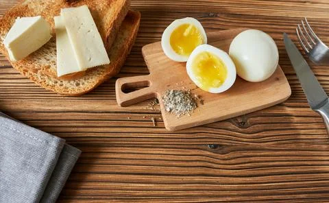 Boiled eggs, butter, bread and a knife on a wooden table. Stock Photos