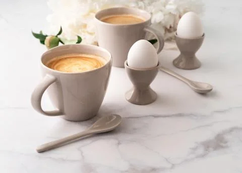 Boiled eggs in ceramic egg cups and two cups of coffee on background of beaut Stock Photos