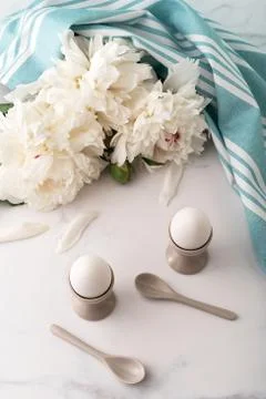 Boiled eggs in ceramic egg cups on background of beautiful white peony and tu Stock Photos