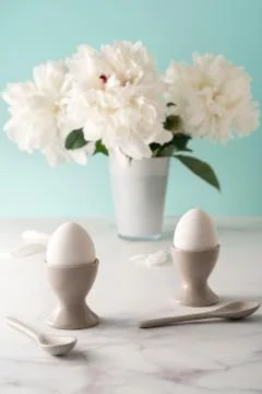 Boiled eggs in ceramic egg cups with ceramic spoons on marble table top Stock Photos