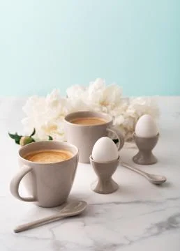 Boiled eggs in ceramic egg cups and two cups of coffee on background of Stock Photos