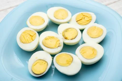 Boiled eggs cut into two halves on a blue plate on a white wooden background. Stock Photos