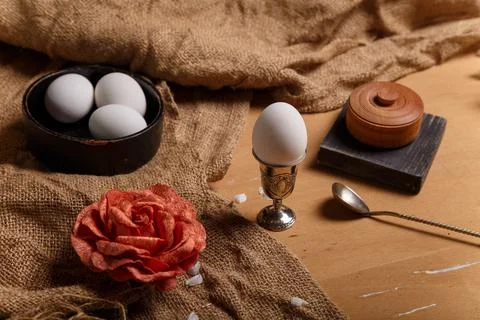 Boiled eggs in egg cup and black bowl, silver spoon, salt pot and fabric rose Stock Photos