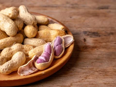 Boiled peanuts in shell with purple violet skin kernels revealed on wooden .. Stock Photos