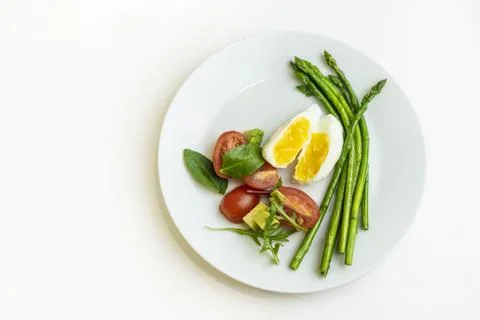 Boiled poached egg, cherry tomatoes, mix salad and asparagus on a white plate on Stock Photos