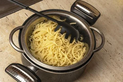 Boiled ready-made spaghetti in a colander and a kitchen saucepan Photos